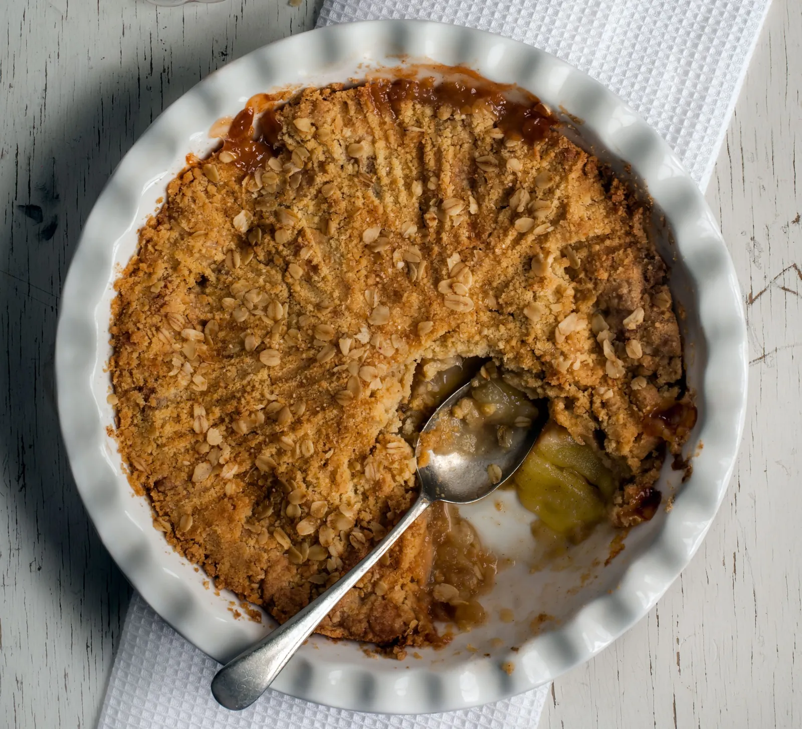 Apple Crumble in weißer Form, ein Löffel hebt weiche Apfelstücke heraus