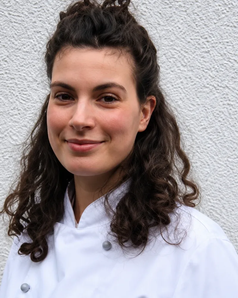 Cora Richardson in weißer Kochjacke vor einer hellen Wand